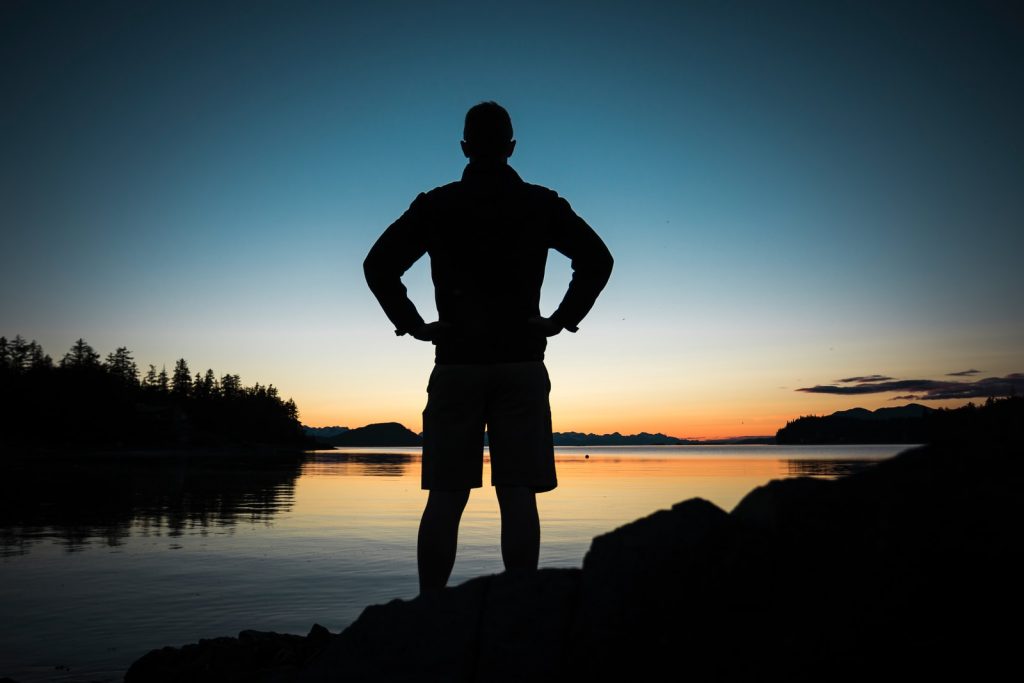 silhouette of man standing near body of water during golden hour