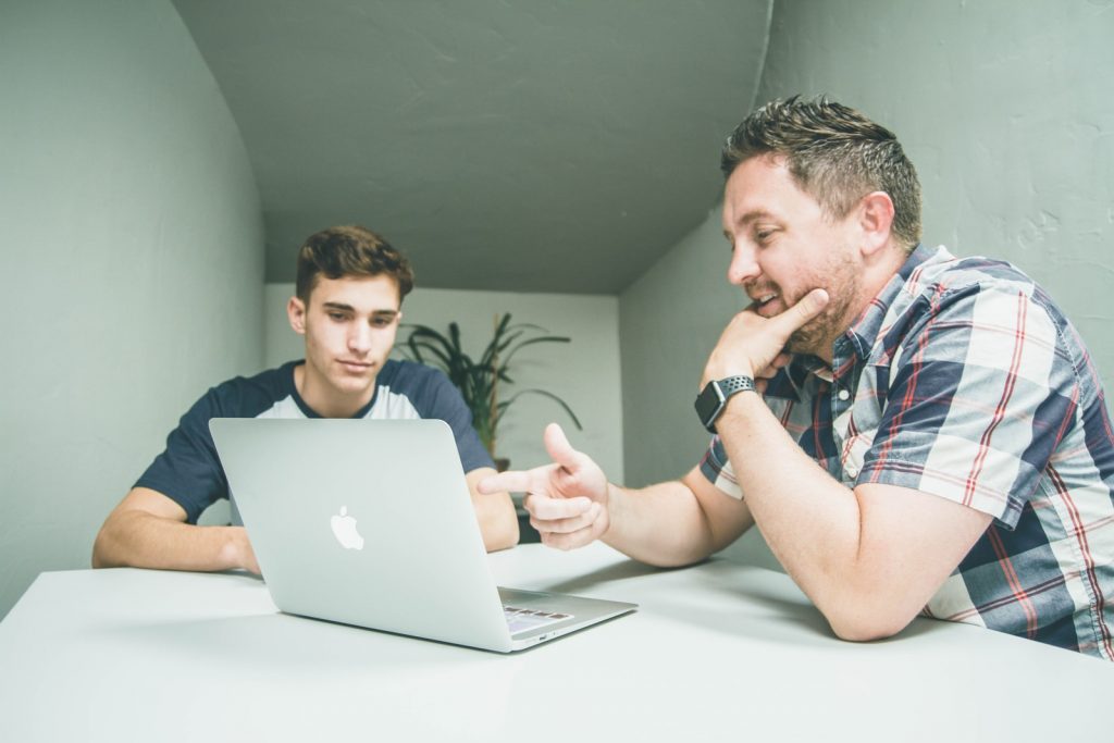 man wearing white and black plaid button-up sports shirt pointing the silver MacBook